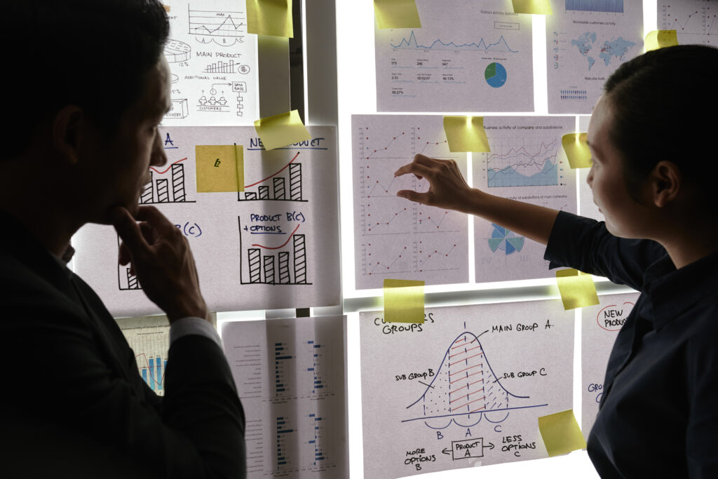 male female colleagues standing by window looking business graphs it